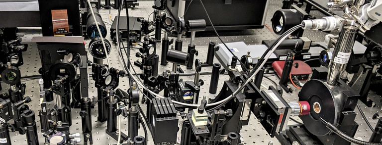 Das Bild zeigt einen (typischen) optischen Tisch in einem Spektroskopielabor. Es befinden sich diverse optische und opto-mechanische Komponenten auf dem Labortisch.