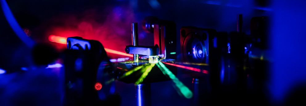 The image shows several laser beams of different colors hitting a beam splitter cube.